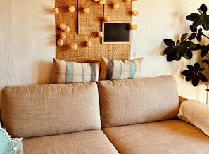 Um sofá com almofadas estampadas, um ornamento de parede trançado e um vaso com planta.