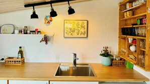 Eine Küche mit Holzarbeitsplatte, Edelstahlspüle, Pendelleuchten, einem gerahmten Pflanzenprint und einem Holzschrank mit Geschirr.