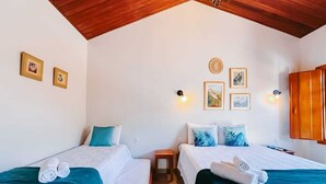 A room with two beds, each with white linens and teal accents, a small wooden nightstand, and wall-mounted artwork. - Pousada Màe Natureza (Pirenópolis)