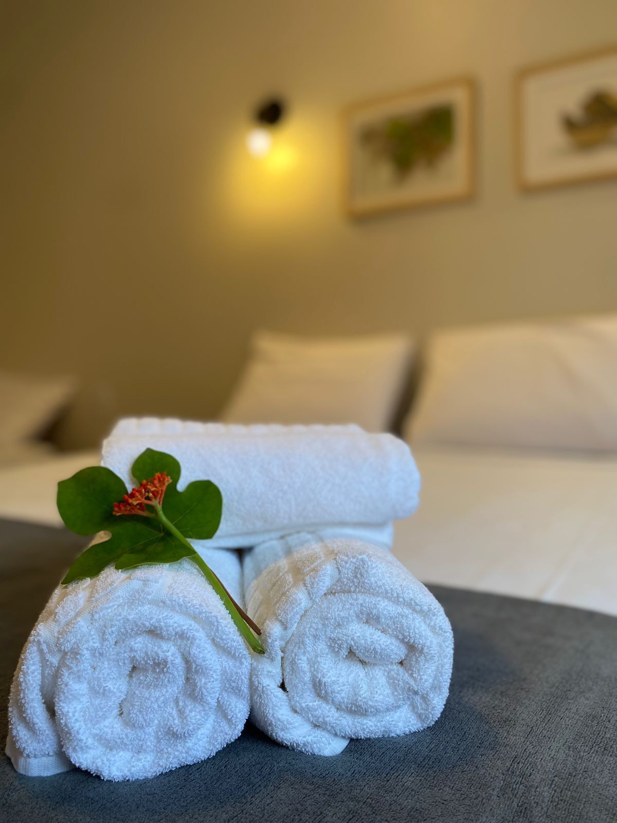 A neatly made bed with white linens and a single rolled towel with a green leaf.