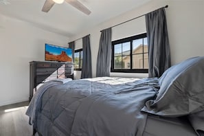A bedroom with a bed, a dresser, a painting, and a window with curtains.