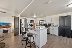 A modern kitchen with a central island, bar stools, a flat-screen TV, and a large window.