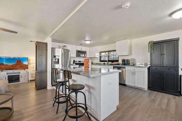 A modern kitchen with a central island, bar stools, a flat-screen TV, and a large window.