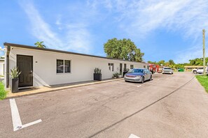 A building with a parking lot, a car, and a red vehicle in the distance.