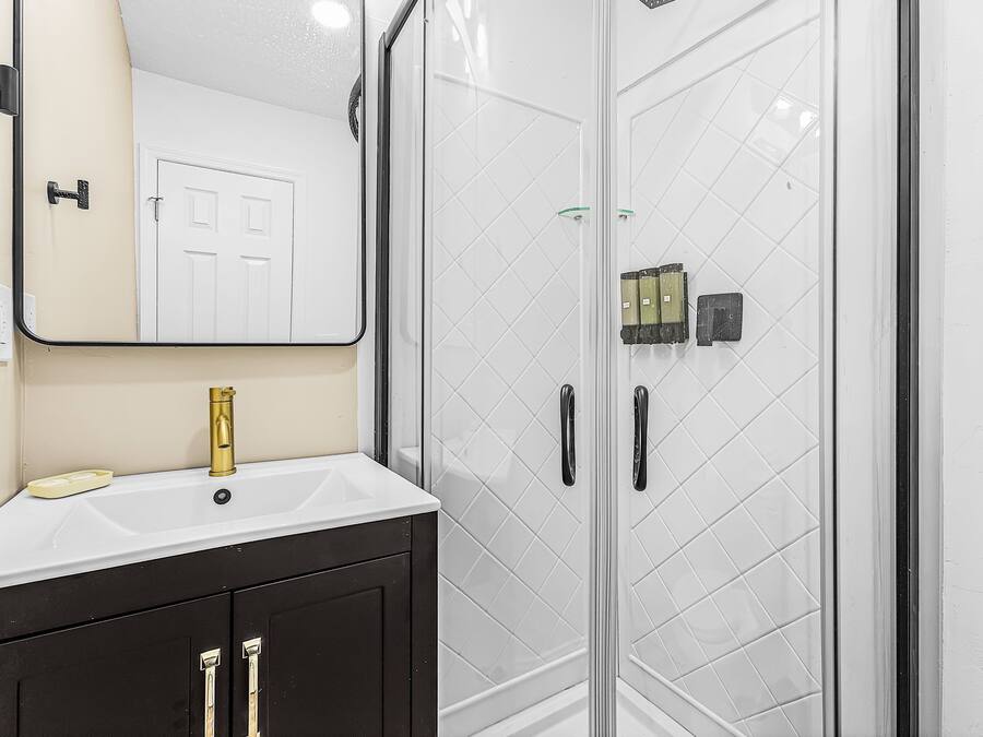 A bathroom with a white sink, a gold faucet, a black vanity, and a glass shower enclosure.
