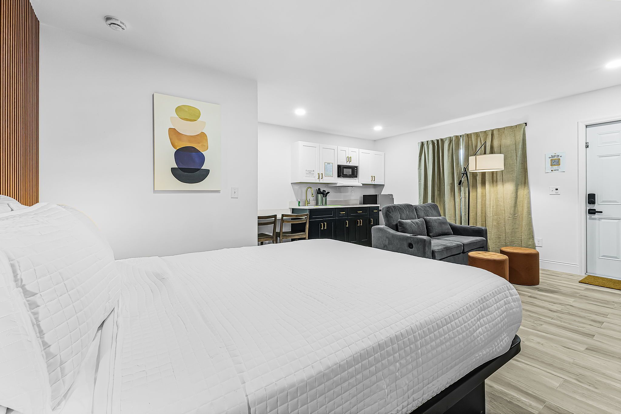 Quarto de hotel com cama, escrivaninha, cadeira, sofá, micro-ondas e porta.