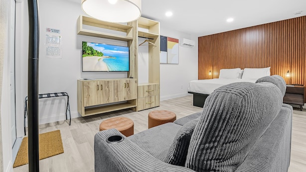 A modern hotel room with a TV, wooden furniture, a bed, and a view of the sea. - Veras Inn & Suites (Fort Myers)