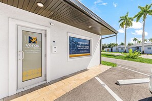 Entrada de hotel con puerta de cristal, cartel y zona de estacionamiento.