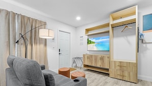 A modern living room with a sofa, ottoman, TV, wooden cabinet, and a hanging light fixture. - Veras Inn & Suites (Fort Myers)