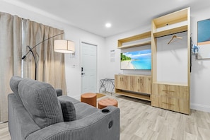 Una sala de estar moderna con sofá, reposapiés, televisor, mueble de madera y lámpara colgante.
