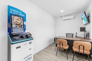 Una habitación con un quiosco de registro, un mostrador con sillas, un televisor de pantalla plana y un equipo de aire acondicionado.