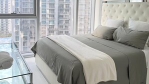 Ein modernes Schlafzimmer mit einem großen Bett, einem Glastisch und Blick auf die Stadt.