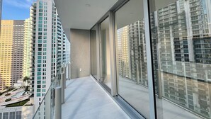 Ein moderner Balkon mit großen Fenstern, einer flachen Dachkonstruktion und Blick auf hohe Gebäude.