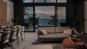 A modern living room with a large window overlooking the sea, a sofa, chairs, and a dining area. - Villa Soho (Starigrad, Paklenica,)