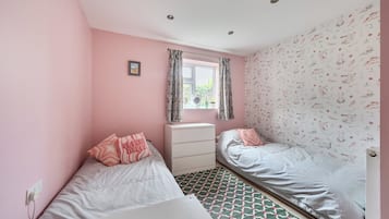 Une chambre avec deux lits, une fenêtre avec des rideaux, un radiateur et un mur orné d’un motif floral.