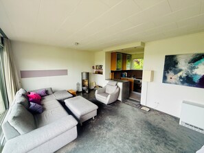 A modern living room with a sectional sofa, a small armchair, a fireplace, and a kitchen area with wooden cabinets.