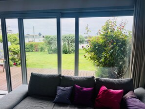 A room with a large window, a grey sofa with cushions, and a view of a garden.
