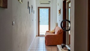 Un passadís amb sòl de rajola, un sofà, un mirall i una porta que dona a una habitació lluminosa.