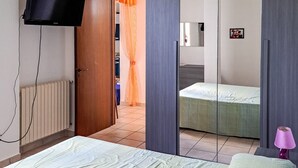 Un dormitori amb un llit, televisió, mirall i una porta que dona a una altra habitació.