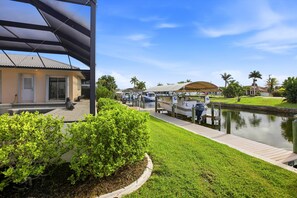 Ein Haus am Wasser mit überdachter Terrasse, Bootssteg und gepflegtem Rasen.