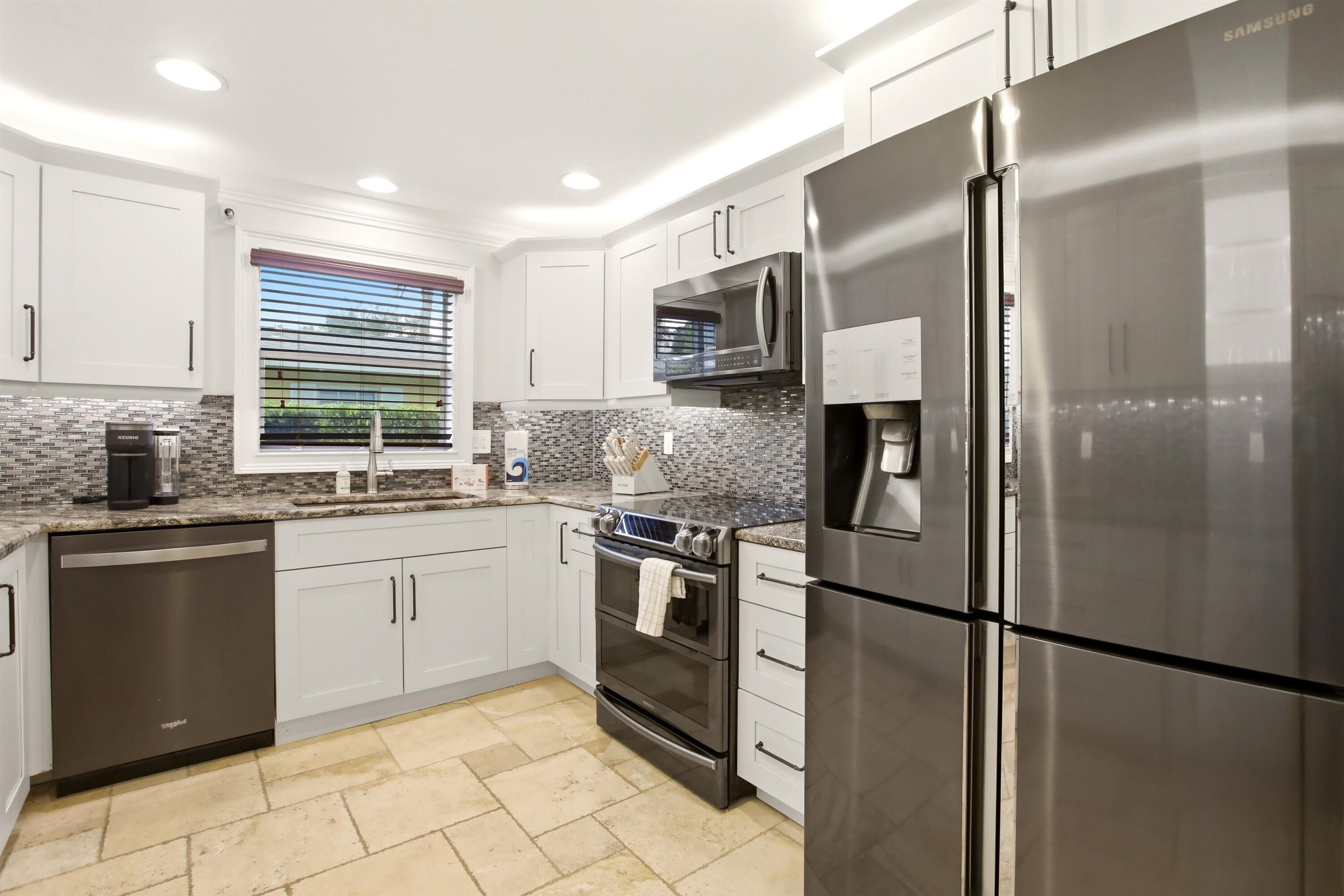 A modern kitchen with stainless steel appliances, white cabinetry, and a tiled backsplash.