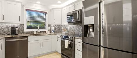 A modern kitchen with stainless steel appliances, white cabinetry, and a tiled backsplash.