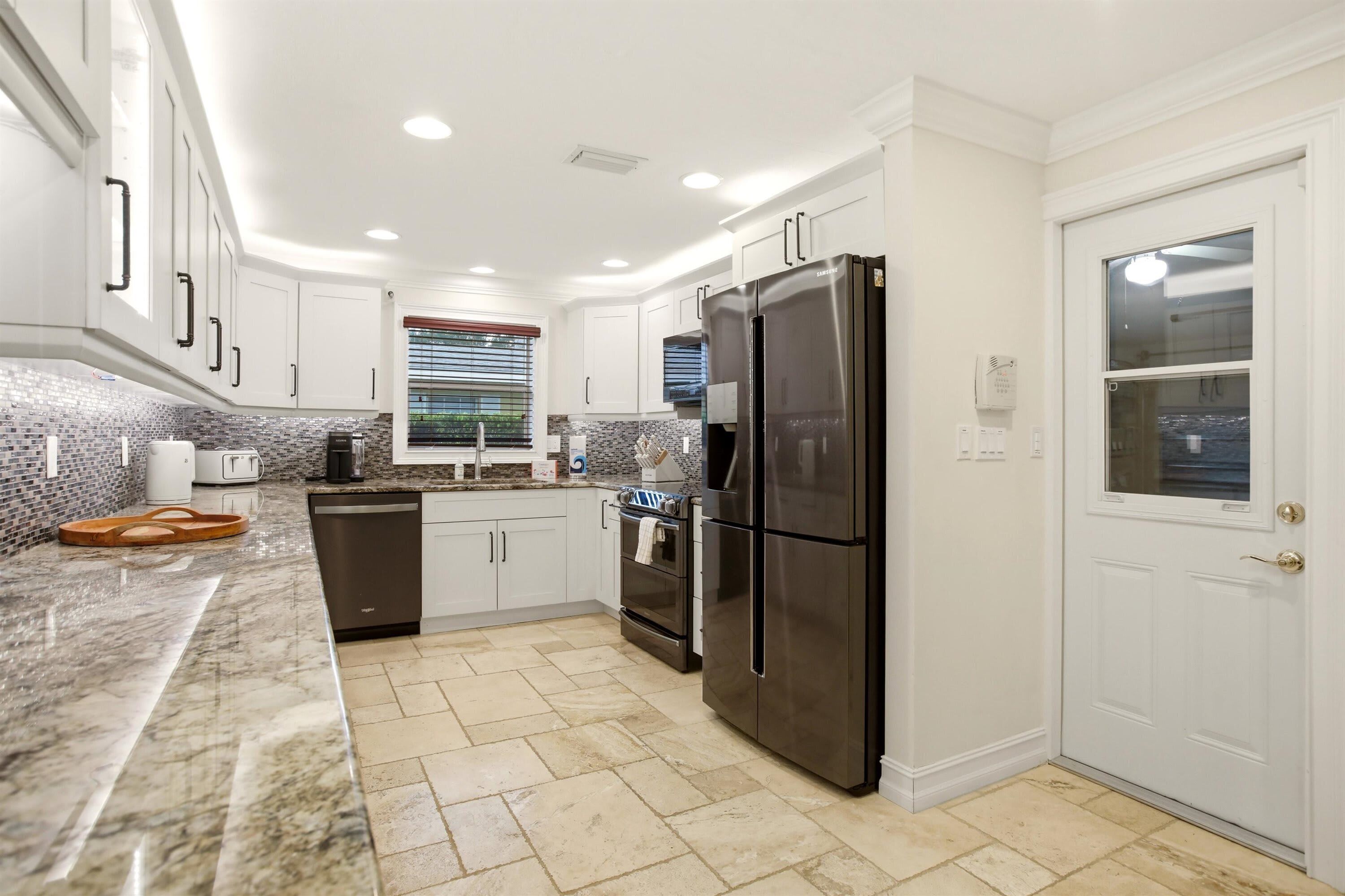 A modern kitchen with white cabinets, a stainless steel refrigerator, a dishwasher, and a tiled backsplash.