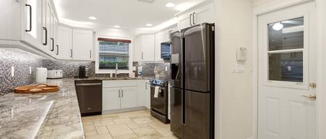 A modern kitchen with white cabinets, a stainless steel refrigerator, a dishwasher, and a tiled backsplash.