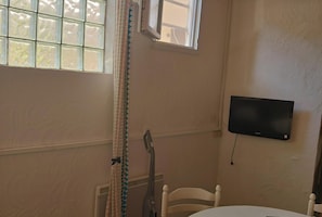 Une pièce avec une fenêtre, un téléviseur fixé au mur, un radiateur et une chaise.