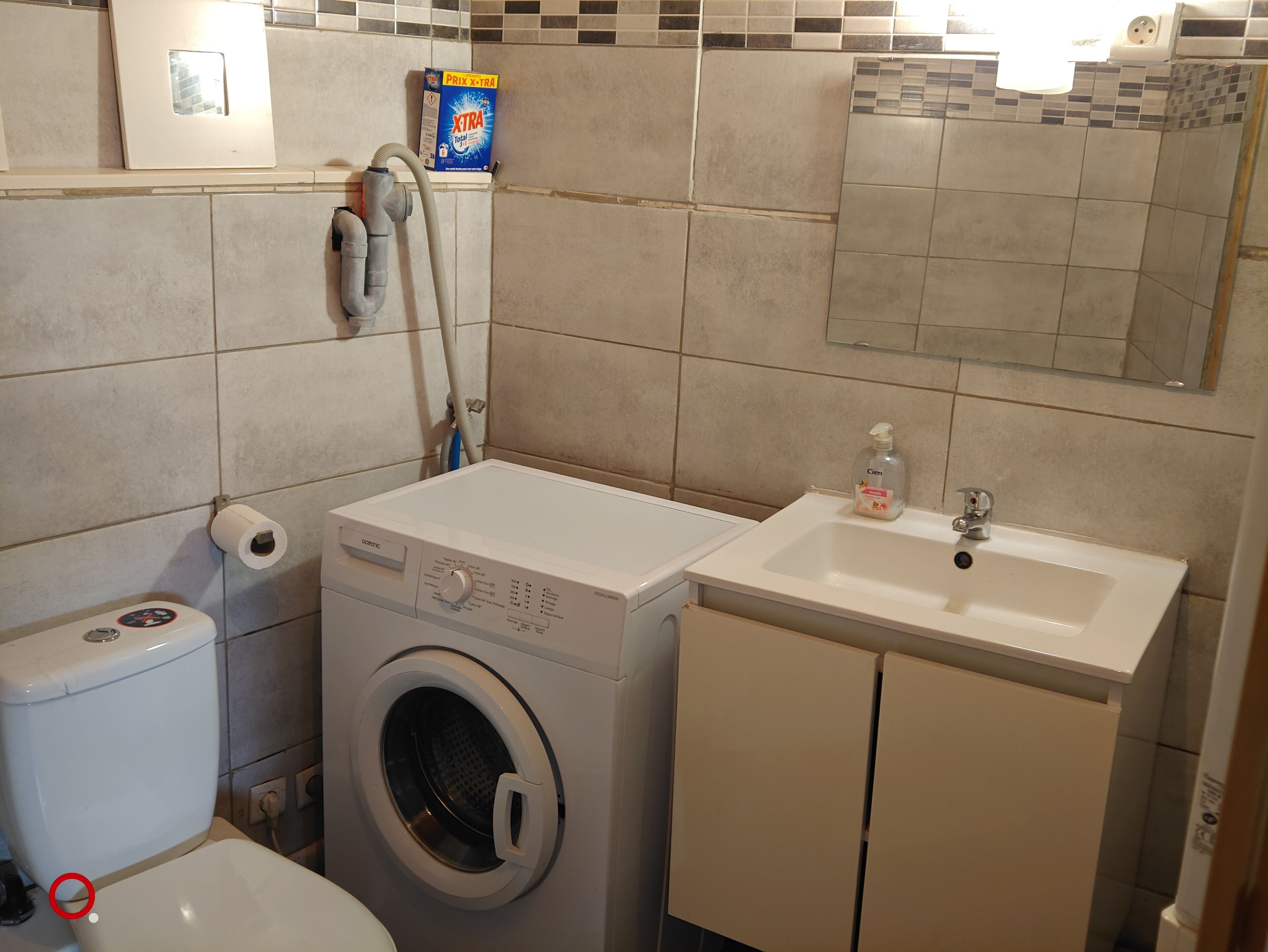 A compact bathroom with a washing machine, toilet, sink, and a tiled backsplash.