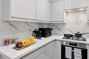 A modern kitchen with white cabinets, a marble backsplash, a gas stove, a coffee maker, and a fruit platter. - Central | FREE parking | Connections to Manchester (Cheshire)