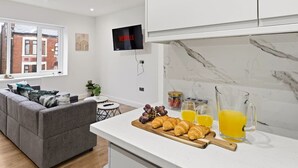 A modern kitchen with a marble countertop, a TV mounted above it, and a dining area with a grey sofa and a small table. - Central | FREE parking | Connections to Manchester (Cheshire)