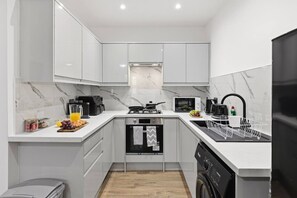 Une cuisine compacte avec des meubles blancs, un four à micro-ondes, une machine à café et un lave-vaisselle.