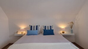 Ein Schlafzimmer mit einem Bett, zwei Nachttischen mit Lampen und einer Vase mit Trockenpflanzen.