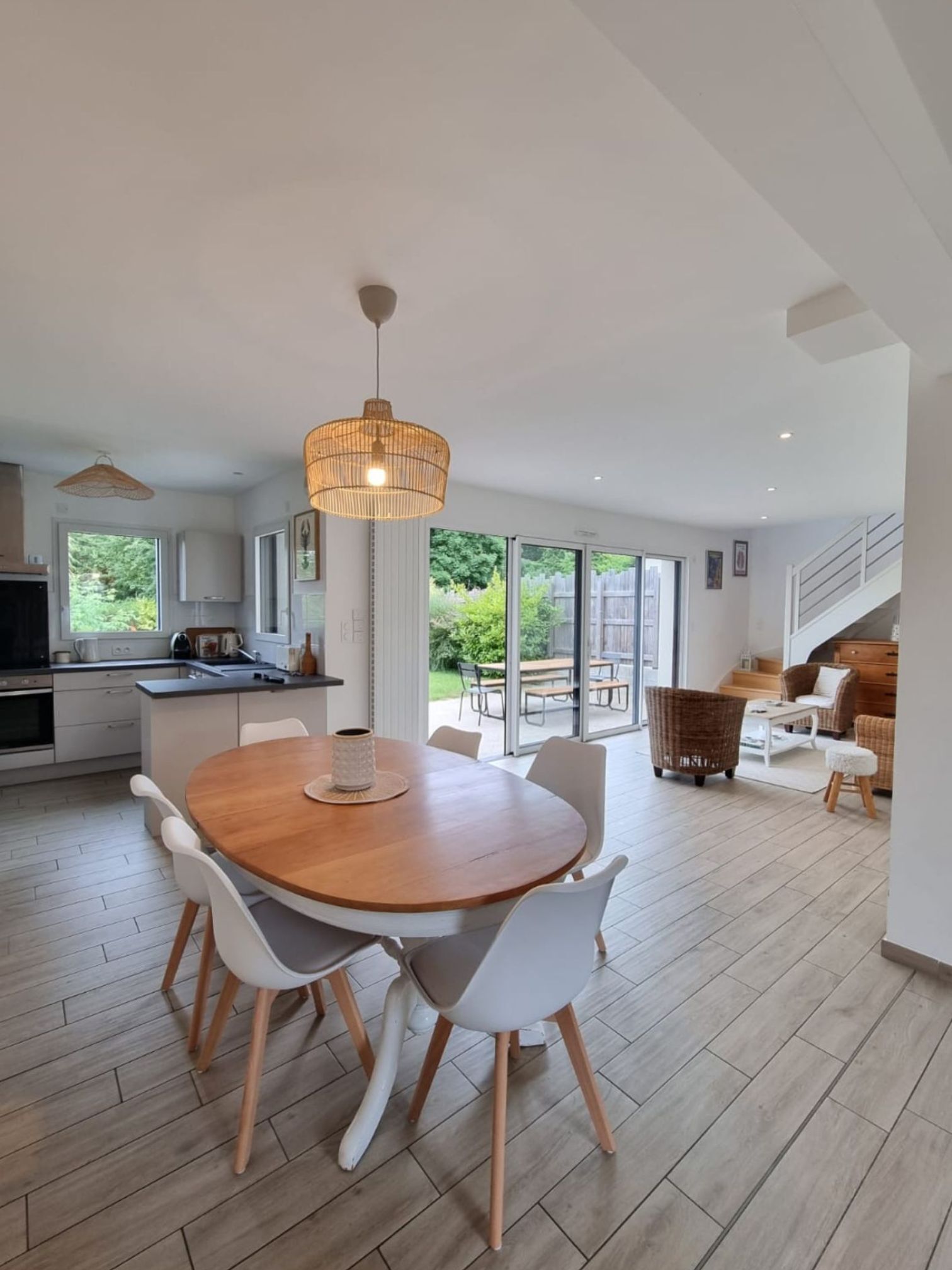 A modern kitchen with a dining area, large windows, and a staircase leading to a loft.