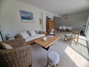 Ein modernes Wohnzimmer mit einer Couch, einem Couchtisch, Korbstühlen, einem runden Hocker und einem Essbereich mit Tisch und Stühlen.