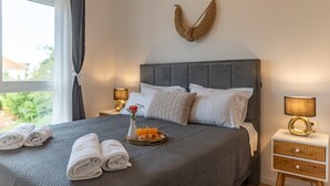 Een netjes opgemaakt bed met kussens, een nachtkastje met een lamp en een raam met gordijnen.
