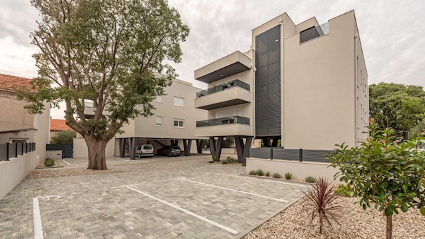 Een modern gebouw met een parkeerplaats, een boom en een kleine tuin.