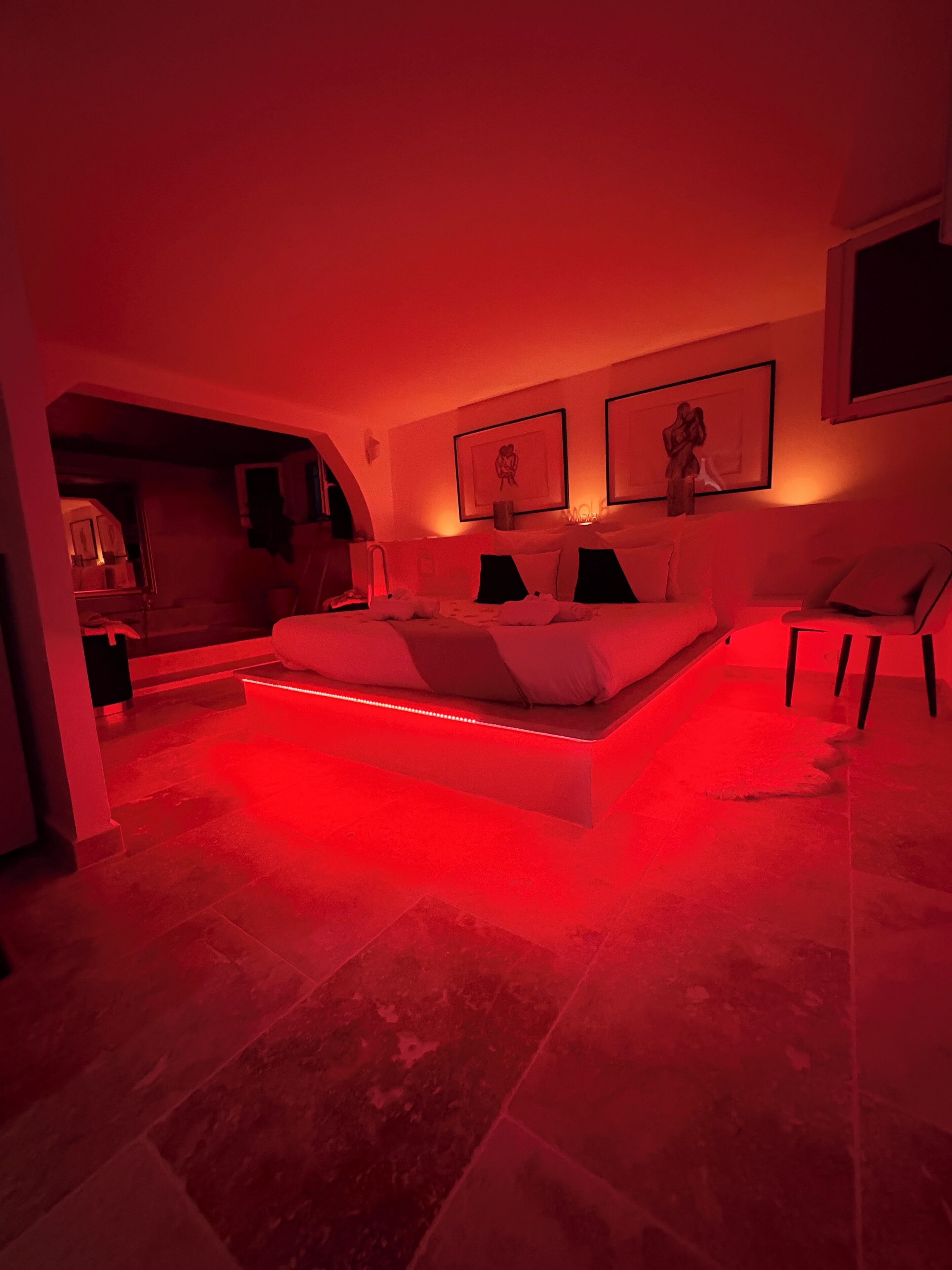 A modern bedroom with a large bed, a seating area, and a view of a kitchen.