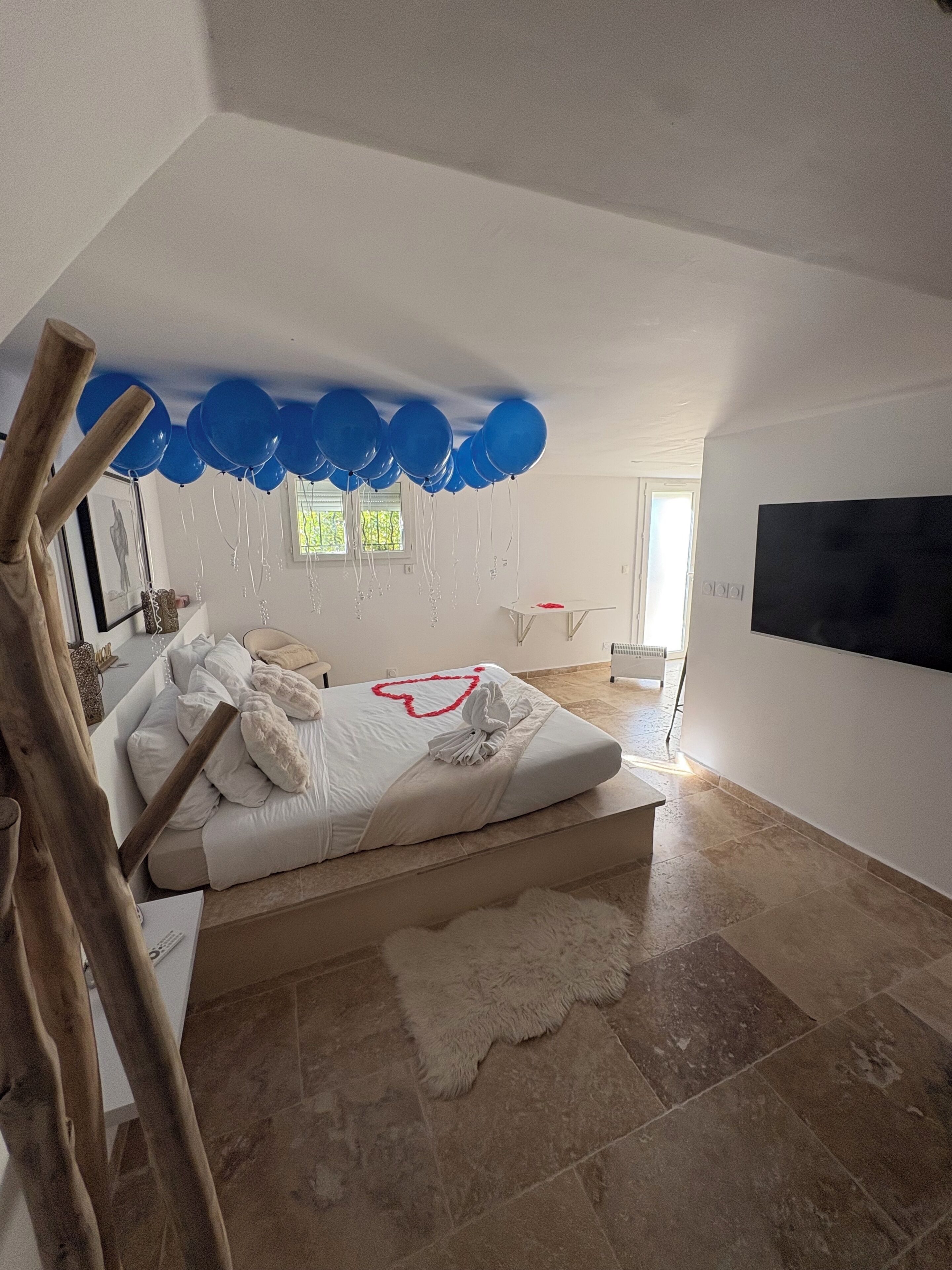 Un dormitorio con cama, televisor, ventana y techo decorado con globos azules.