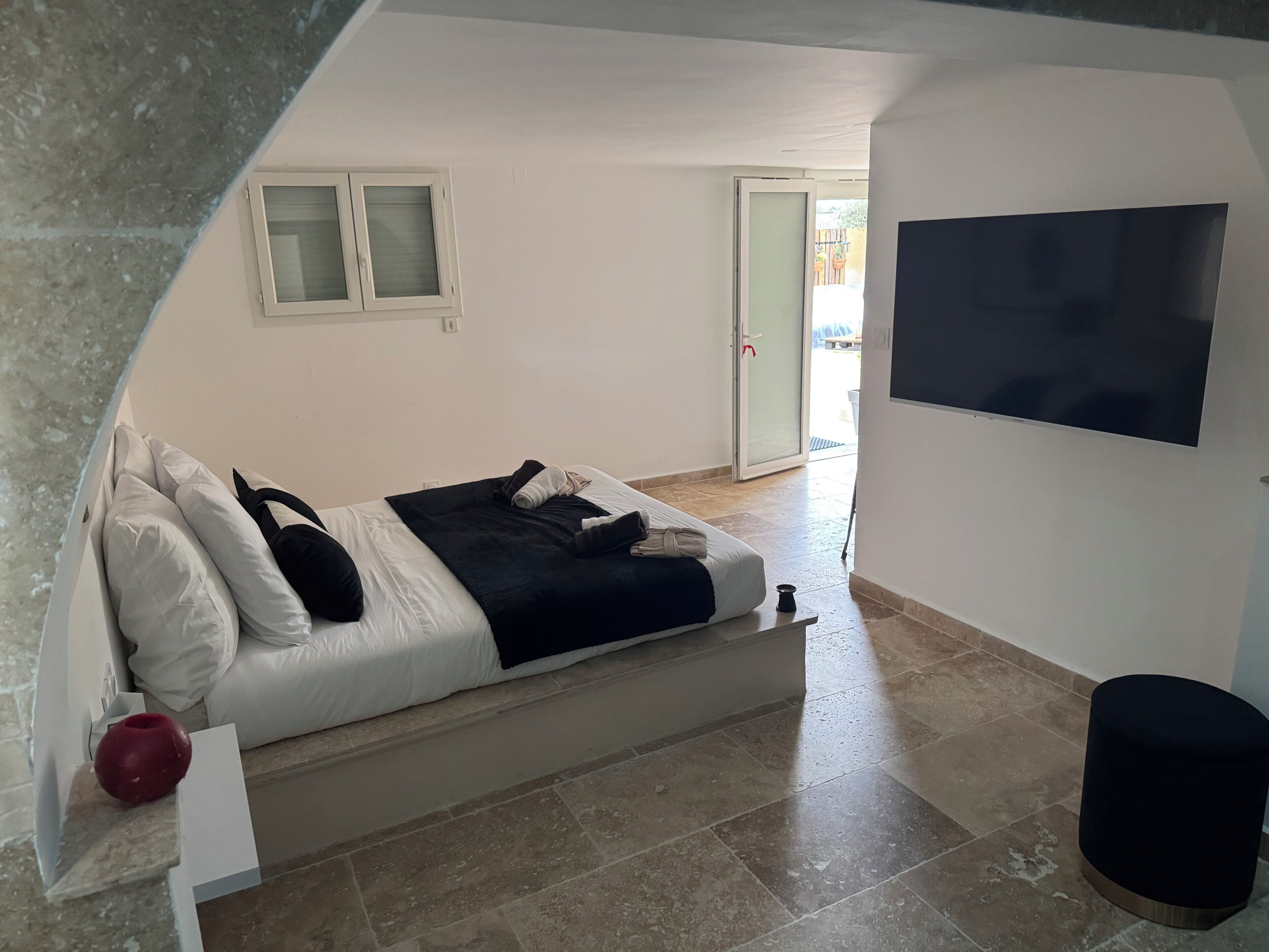 A bedroom with a bed, a TV, a sliding door, and a small stool.
