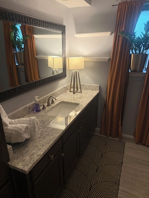 A bathroom with a granite countertop, a sink, a mirror, a towel, a lamp, and a patterned rug. - FIFA WORLD CUP Marvelous 2-bedroom house with Kitchenette in charming Arlington (Arlington)