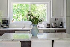 A modern kitchen with a marble island, a vase with flowers, and a view of greenery through the window.