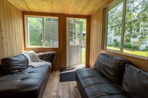 A cabin interior with two leather couches, wooden walls, large windows, and a door leading outside.