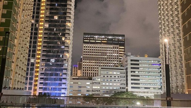 A nighttime cityscape with high-rise buildings and a reflective water body.