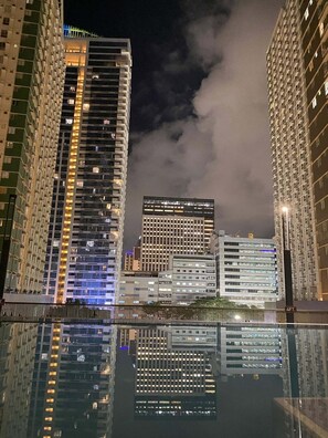 Une vue nocturne d’une ville, avec de hauts immeubles et une étendue d’eau qui reflète la lumière.