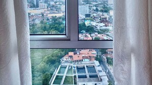 A window with a view of a cityscape, including buildings and greenery.