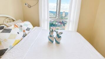 A bedroom with a bed, a window with curtains, an air conditioning unit, and a view of a cityscape.