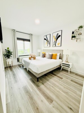 Ein Schlafzimmer mit einem Bett, Nachttischen, einem Fenster und Kunstwerken an der Wand.