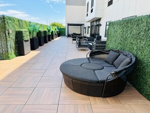 Um terraço no telhado com uma área de estar em curva, uma pérgola e uma fileira de floreiras na borda.